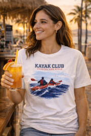 Woman wearing the white Kayak Club coastal T-shirt while holding a drink at a beach bar.