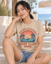Woman seated near the beach wearing the Sand Malibu Surf Club graphic T-shirt