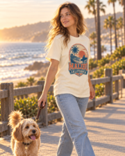Woman wearing the ivory Malibu California Surf Tee while walking her dog on a coastal path at sunset