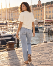 Back view of a woman wearing the ivory Saint-Tropez Côte d'Azur tee, walking along the Saint-Tropez quay