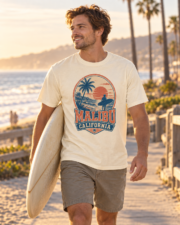 Man wearing the ivory Malibu California Surf Tee while carrying a surfboard by the beach at sunset