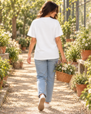 Woman walking through a greenhouse in a white Comfort Colors tee shown from the back