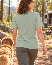 Back view of a woman wearing the plain Bay Trail Club tee beside a pine forest campsite.