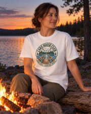 Woman in the White Lake House Club Crest T-shirt by a lakeside campfire at dusk