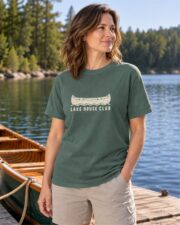 Woman in the Blue Spruce Lake House Club Canoe T-shirt on a dock beside a wooden canoe