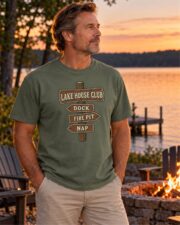 Man wearing the Moss Lake House Club Signpost T-shirt by a lakeside fire pit at sunset