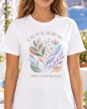 Close-up of a woman wearing a white Calm & Serene t-shirt with a pastel watercolor botanical graphic and the words Find Your Balance, on a sunny Mediterranean terrace