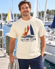 Man wearing the Ivory Sailing Club Regatta T-shirt on a dock with sailboats behind