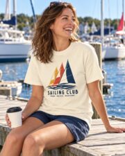 Woman in the Ivory Sailing Club Regatta T-shirt sitting on a dock with a coffee